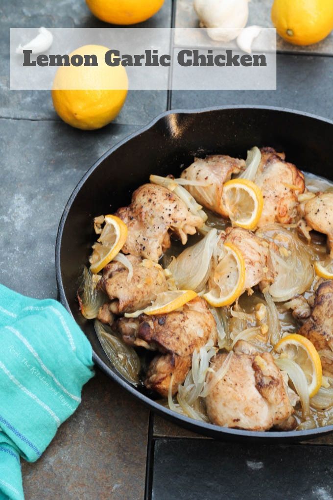 chicken thighs in cast iron pan with lemon and onion, lemon on table and blue towel around pan handle