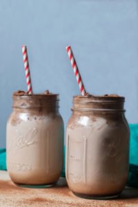 whipped chocolate milk in pint jars with red striped straw and teal cloth in background