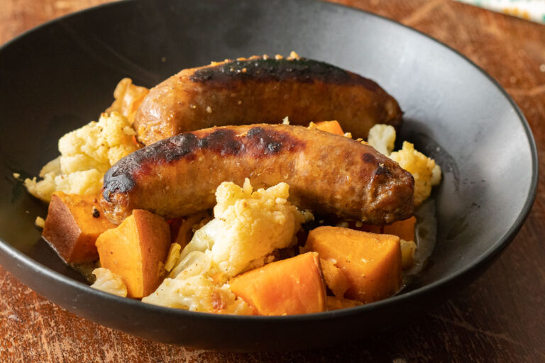 black bowl with 2 sausage links, cubed sweet potatoes and cauliflower florets